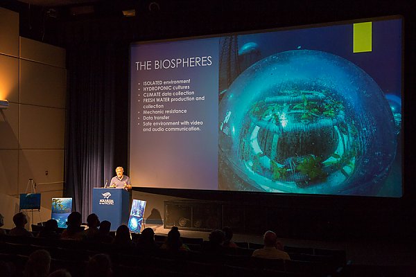 Guest lecturer in front of audience with large graphic on screen.